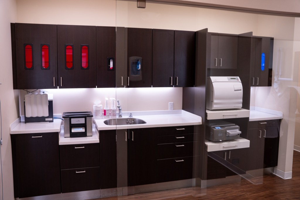 Instrument processing area featuring dark cabinets with red accent lighting, white countertops, sterilization equipment, and organized storage systems.
